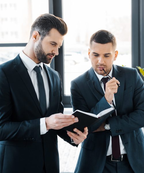 handsome businessman holding notebook near colleague in modern office